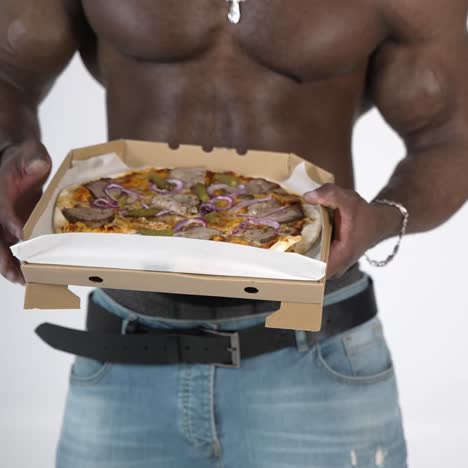 male torso of african athlete. young muscular african man with naked torso eating pizza in studio