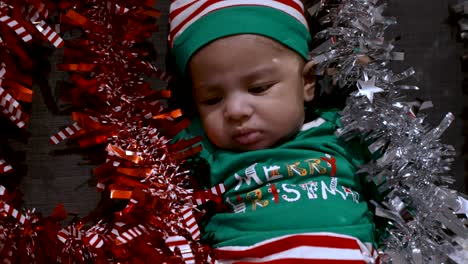 adorable 2 month old baby boy wearing green merry christmas shirt and hat surrounded by red and silver tinsel