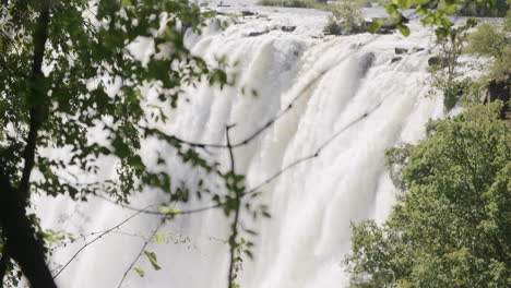 Panning-slow-motion-footage-of-a-waterfall-from-behind-the-branches-of-a-tree