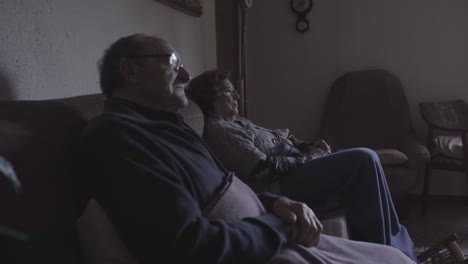 Senior-couple-sitting-on-the-sofa-at-home-while-watching-tv