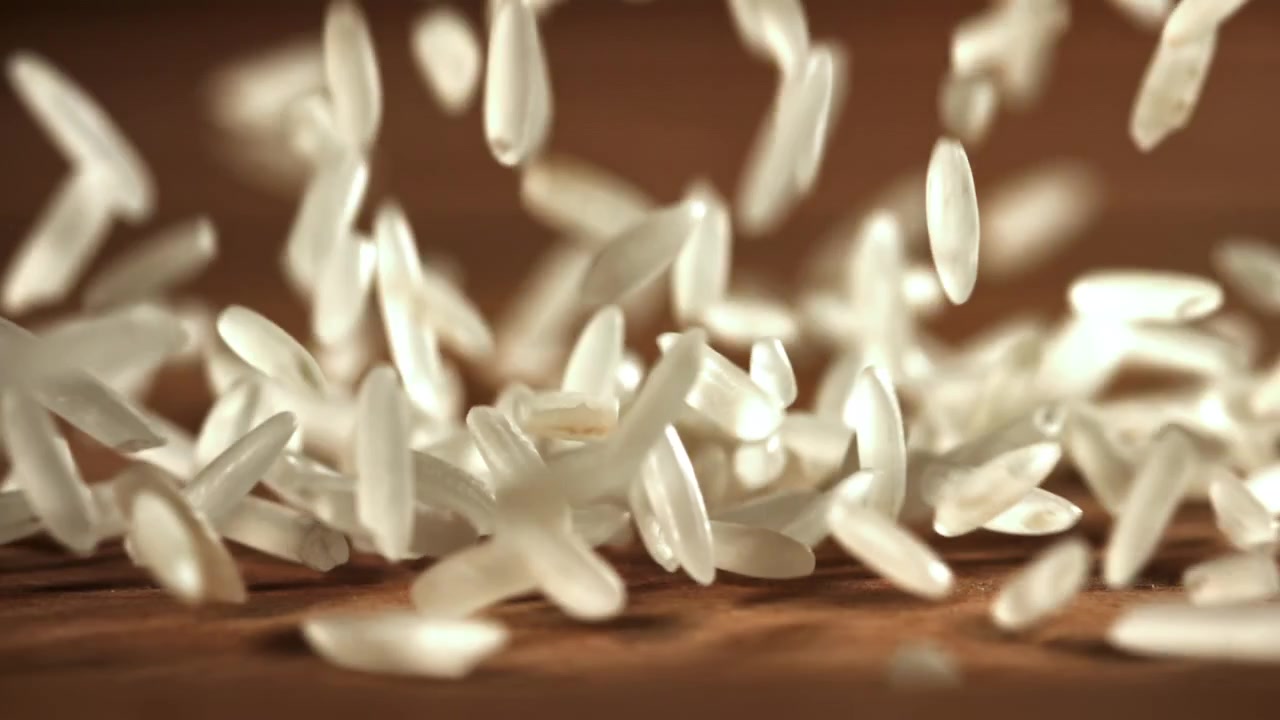 Hvide risgryn, der falder ned på en træoverflade i slowmotion.