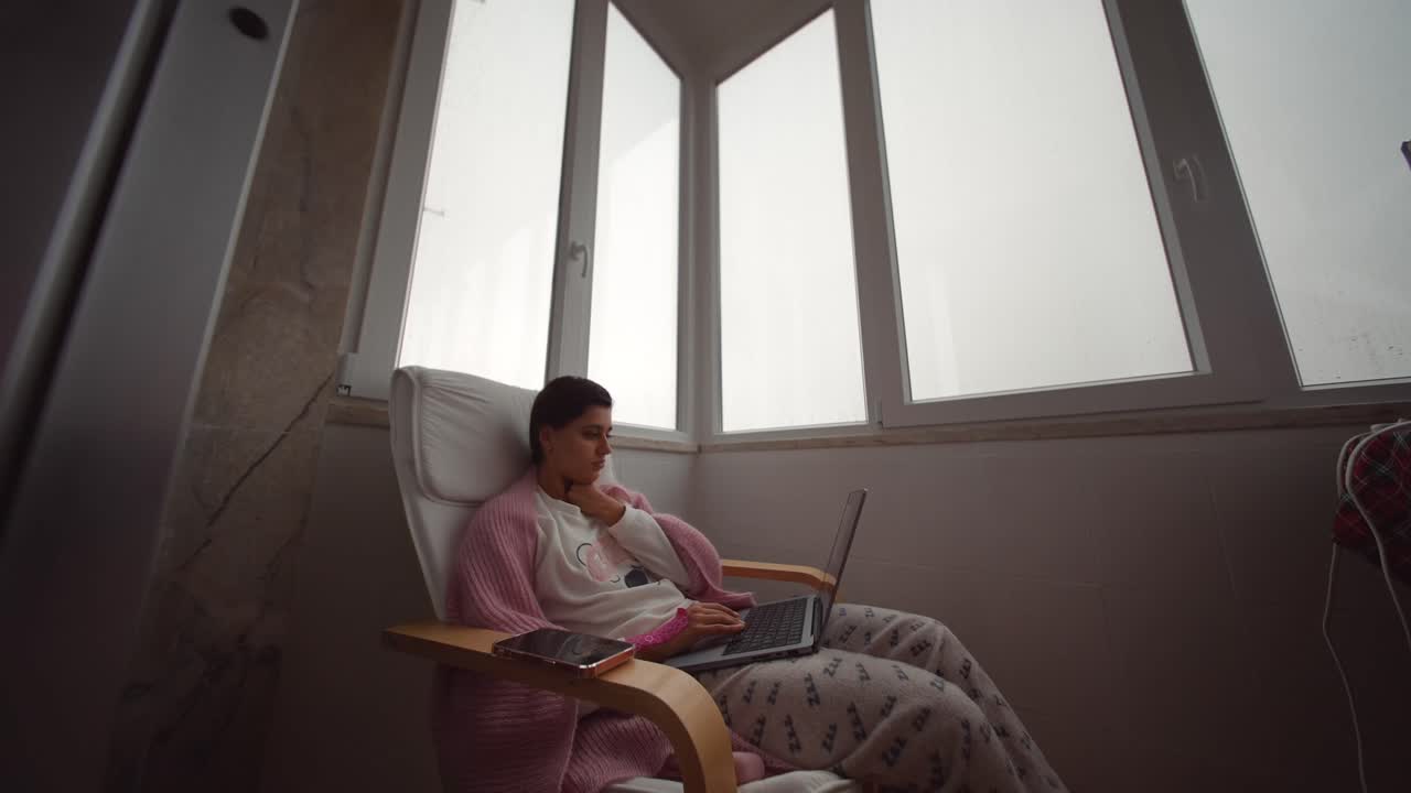 Donna che lavora al computer portatile su una sedia vicino alla finestra