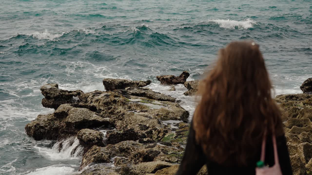 A woman stands on the rocks watching waves break along Tangier’s rugged coastline