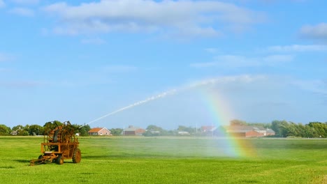 Eine-Maschine,-Die-Wasser-Auf-Das-Gras-Auf-Dem-Boden-Sprüht,-Mit-Einem-Wunderschönen-Regenbogen-Im-Hintergrund