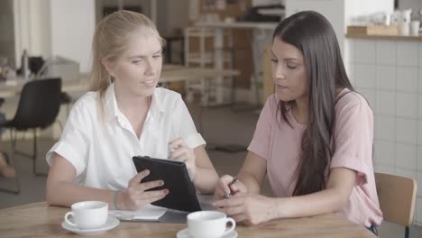 mujeres empresarias seguras de sí mismas mirando la tableta y discutiendo el proyecto