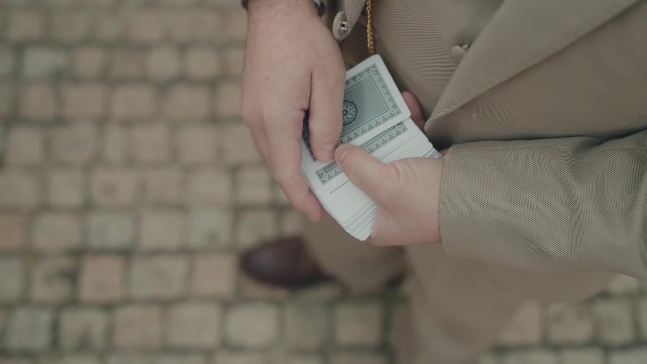 Close-up van handen die speelkaarten hanteren tijdens een truc op een geplaveide straat.