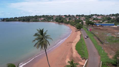 Aerial-establishing-shot-of-São-Tomé-e-Principe-Island,-Cars-passing-by-a-turquiose-colored-beach