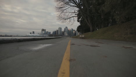 Wide-low-angle-shot-of-Seawall-trail-with-yellow-line-and-Vancouver-skyline-in-background,-Morning,-Slowmo