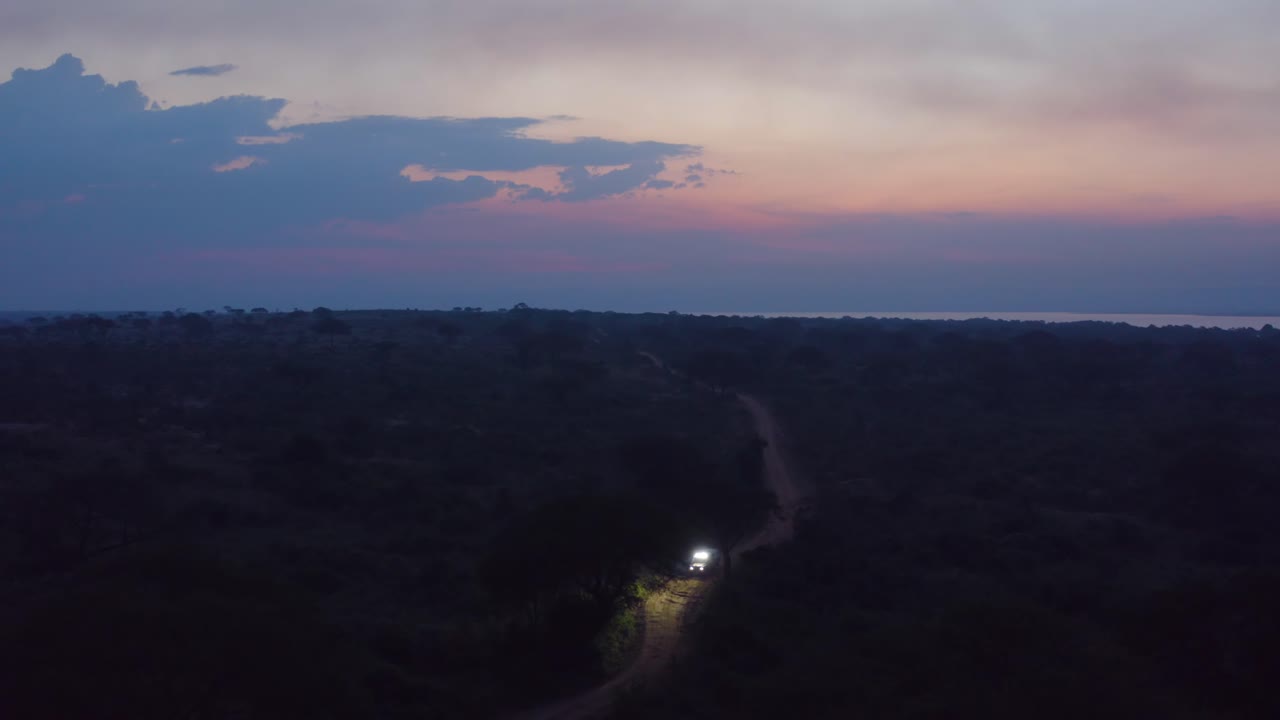 el coche conduce por un estrecho camino de tierra en el desierto de uganda al atardecer con luces brillantes