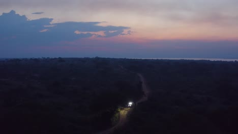 car drives down narrow dirt road in ugandan wilderness at sunset with bright lights