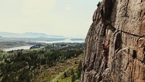 Strong-girl-climbing-rocky-wall-in-Norway,-aerial-panoramic-view