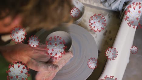 Composite-video-of-covid-19-cells-floating-against-close-up-of-hands-working-on-pottery-wheel