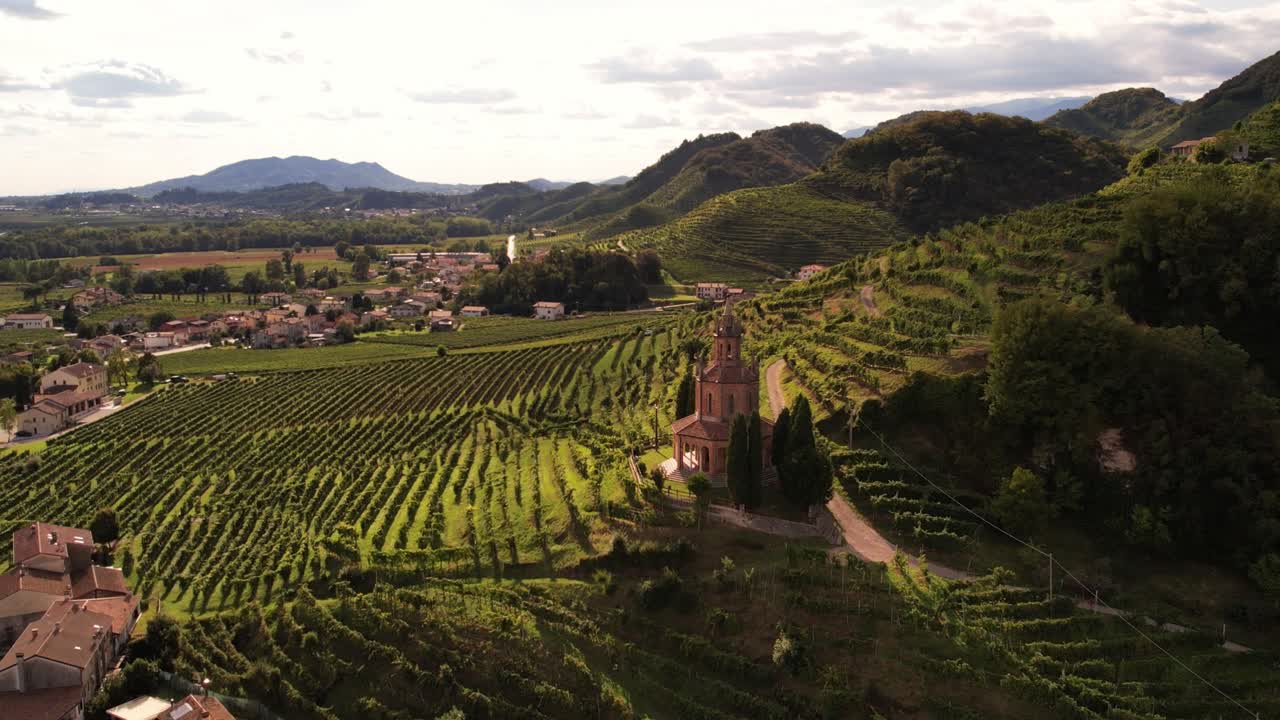 Aerial landscape view of the famous prosecco hills with vineyard rows and a historic church, in Italy