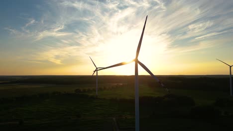 large wind turbines with blades in field aerial view bright orange sunset blue sky wind park slow motion drone turn