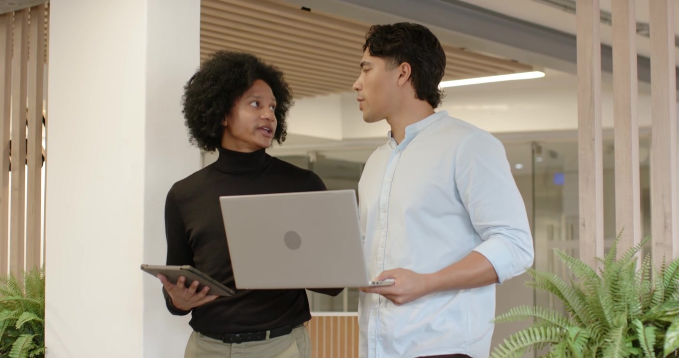 Diverse male peers in smart casual entering left holding tablet laptop at office stopping aligning