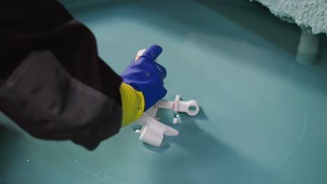 a worker in protective gear carefully arranges white plastic components on a cyan surface