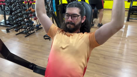 homem latino com barba e cabelo longo realizando exercício de pressão de ombro