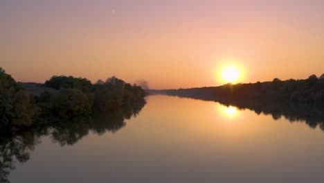 drone footage in the sunset, flying above river with beautiful forest around