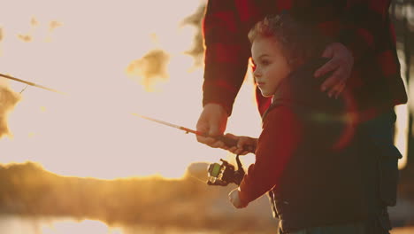 Un-Niño-Lindo-Está-Pescando,-Su-Padre-O-Su-Abuelo-Están-Ayudando-A-Un-Niño-A-Descansar-Activamente-En-La-Naturaleza-A-Pescar-En-El-Lago