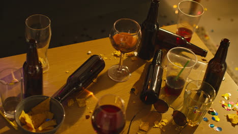 overhead shot of messy table covered with empty wine glasses with beer bottles and snacks after house party 1