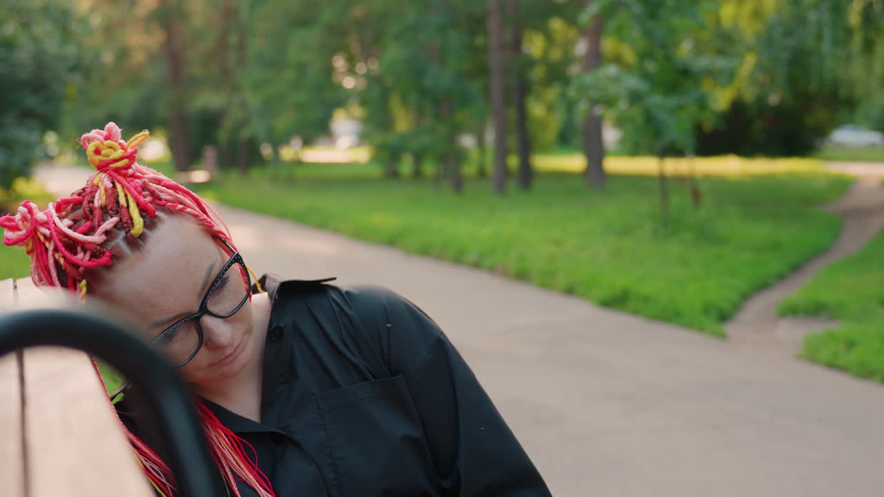 저녁 공원에서 휴식을 취하는 사람, 다채로운 머리카락과 나무가 있는 조용한 저녁 풍경, 선명한 땋은 머리를 한 사람이 석양 아래 평화로운 공원에서 쉬는 고요한 순간