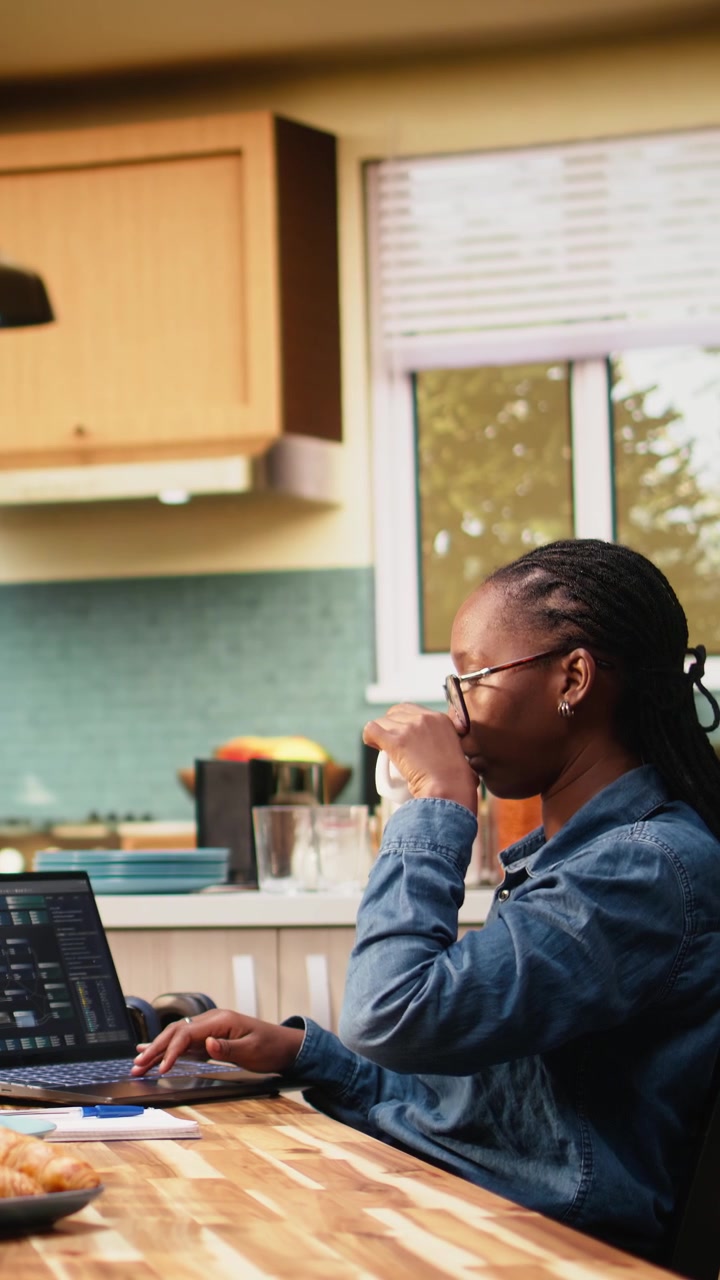 Vertical Video Black woman programming on laptop in kitchen representing hybrid work
