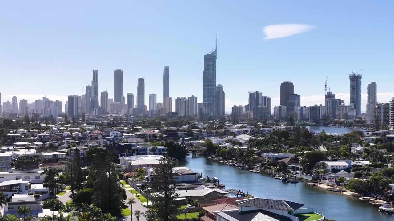 Ripresa con drone che si alza sopra i canali suburbani verso uno skyline moderno di grattacieli sotto cieli azzurri e sereni.