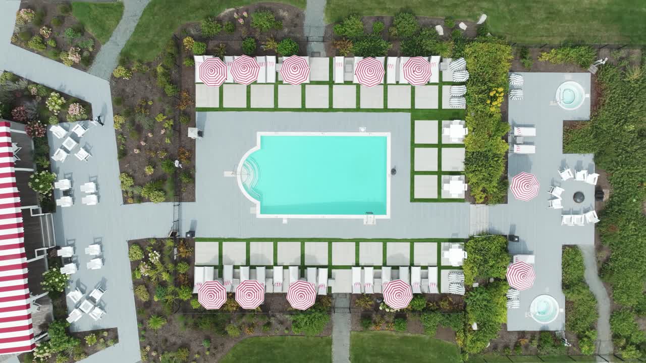 Top-down aerial view of a stylish hotel pool with red-striped umbrellas, lounge chairs, and landscaped gardens—symmetrical luxury outdoor space.