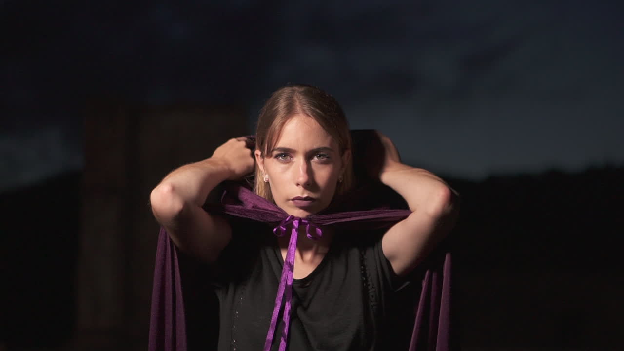 그녀의 머리에서 망토 remiving 후드를 착용하고 카메라를 응시하는 신비한 판타지 여성