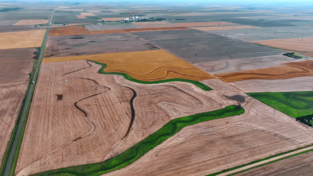 Approaching agricultural fields prepared for sowing plants. Narrow green areas and channels with water are in the farms. Top view.