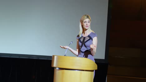 joven mujer de negocios caucásica hablando en el escenario en el auditorio 4k