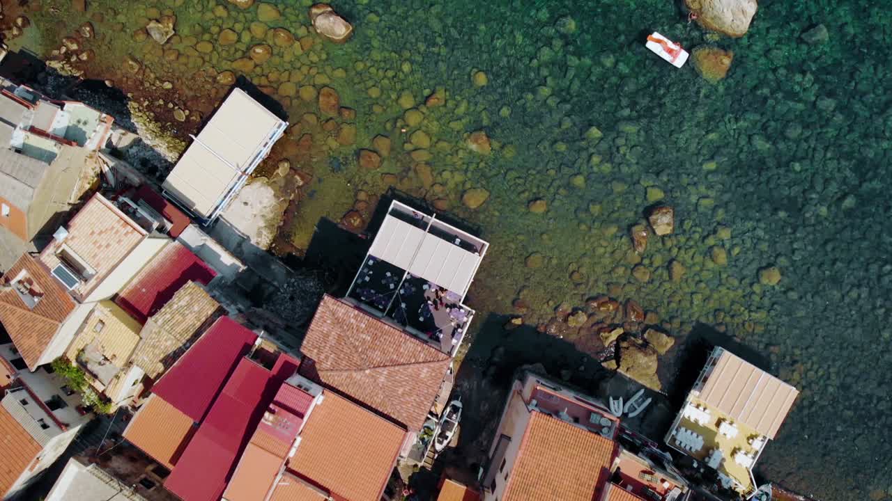 Aerial, top down, drone shot above buildings on the coast of the Scilla town and boats in turquoise sea, sunny day, at the Tyrrhenian sea, in Calabria, Italy