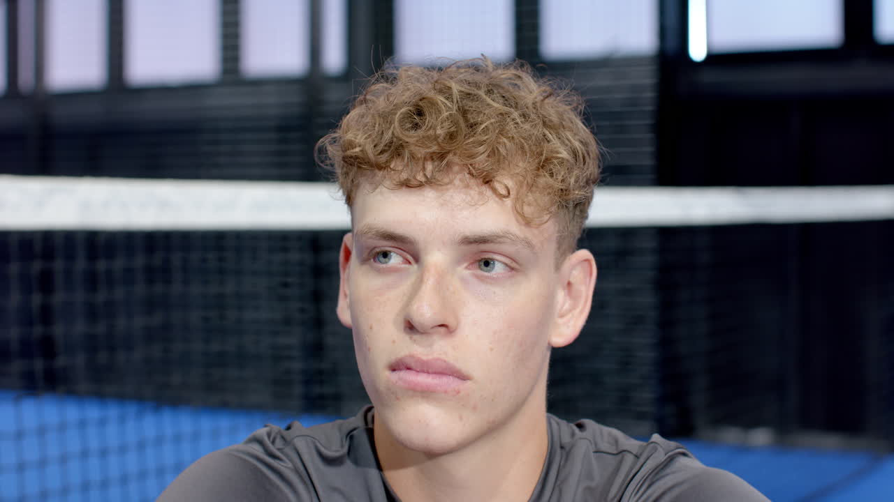 Young man with curly hair focusing during padel tennis match on indoor court, copy space