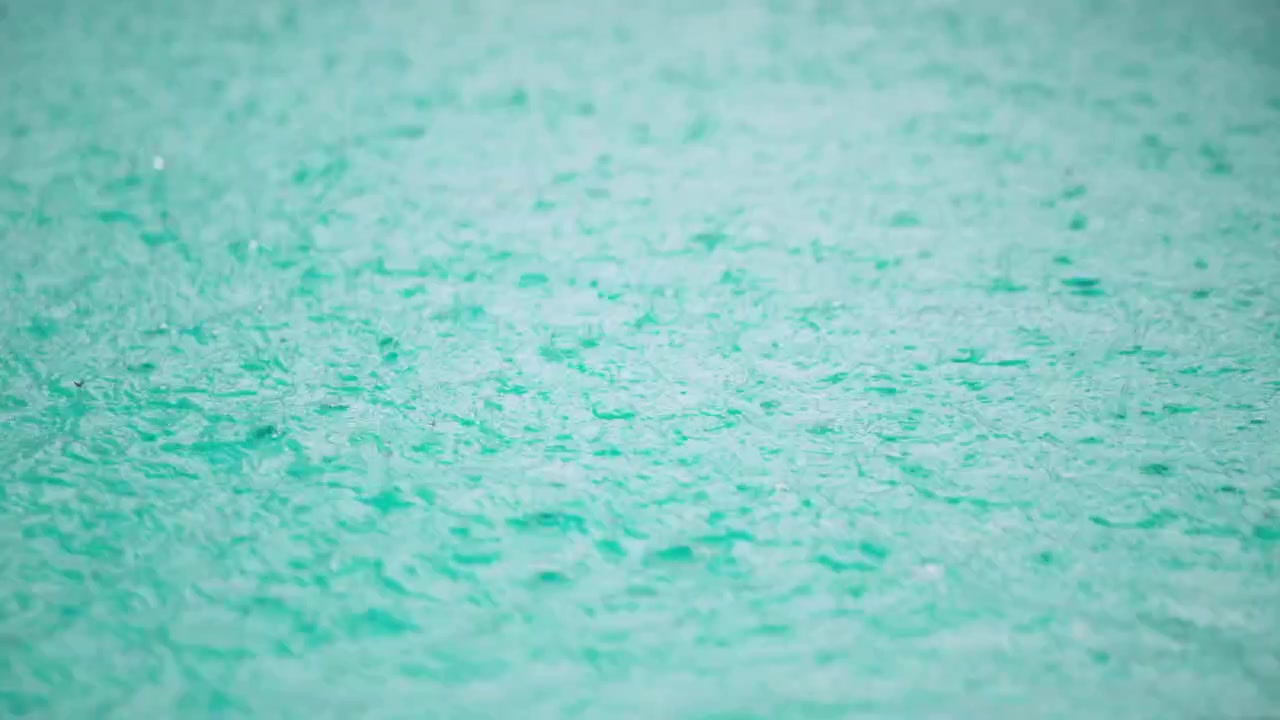 Primo piano al rallentatore della pioggia che colpisce la superficie di una piscina, creando turbolenze, increspature e onde.