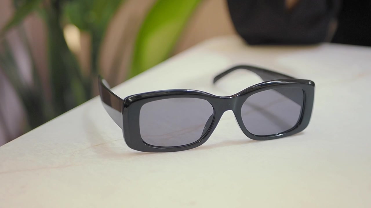 Hand Picking Up Black Sunglasses From A White Table