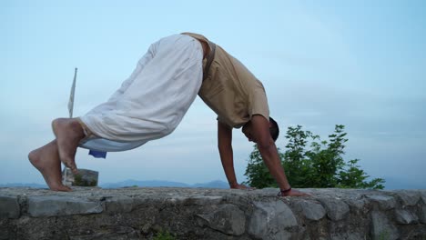 hombre indio practicando su postura de hatha yoga en la parte superior de una pared de piedra al amanecer