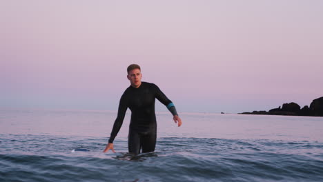 Mann-Im-Neoprenanzug-Hält-Schwimmendes-Surfbrett-In-Der-Hand,-Während-Er-Durch-Die-Wellen-Geht