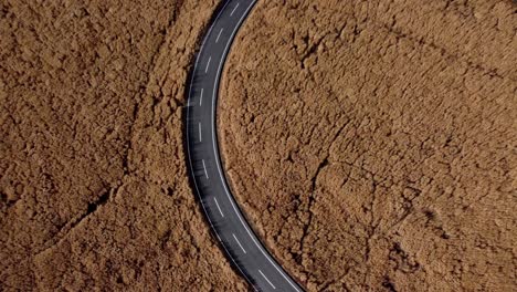 Curved-road-slicing-through-arid,-cracked-earth,-drone-shot-in-bright-daylight