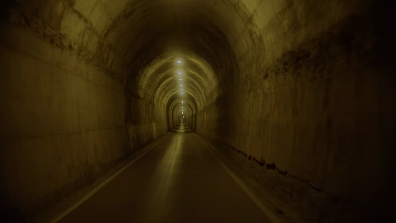 Guida in soggettiva attraverso un lungo tunnel buio con luci.