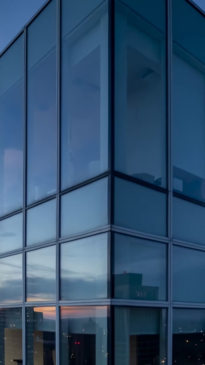 Vertical video: Camera moving down glass corner tower showing sunset glow and chair, dusk falling