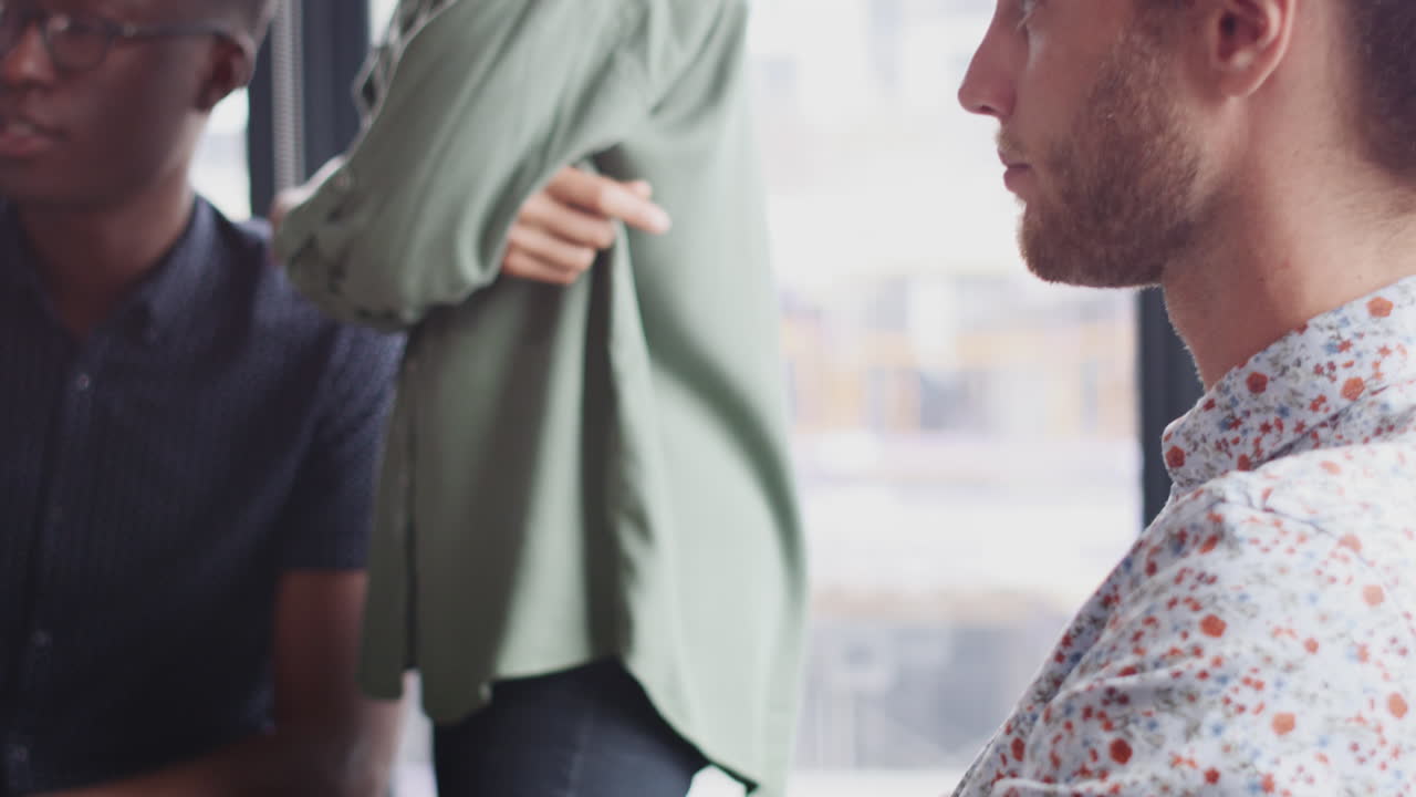 백인 남성 크리에이티브가 컴퓨터에서 일하고, 동료들이 배경에서 일하며, 근접 촬영, 기울기 촬영