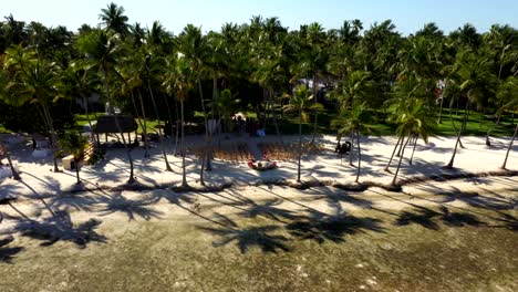 angled aerial orbit above water to resort clearing and bordering trees with charis arranged for wedding