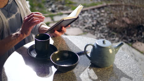 close up on a woman reading a book and drinking a hot cup of herbal green tea