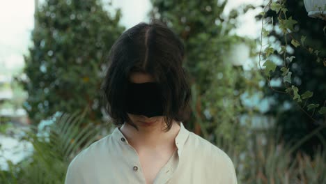 portrait dolly-in cinematic video of a young man blindfolded looking at camera in a greenhouse of plants