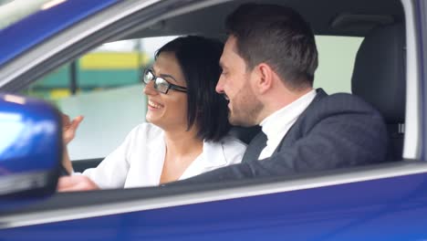 stylish man sitting in car salon and talking with female car dealer. professional helping client to choose best automobile in showroom