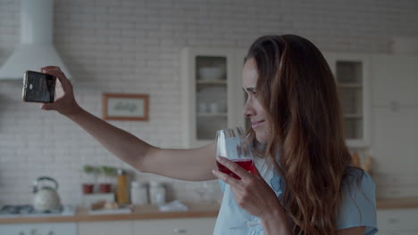 mujer joven tomando una foto selfie con un vaso de vino en el teléfono en el interior de la cocina