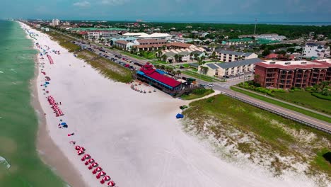 Pompano-Joes-Restaurant-In-Destin,-Florida,-Weit-Weg,-Schwenk-Nach-Links,-Luftaufnahme-Einer-Drohne-Mit-Blick-Auf-Liegestühle-Und-Sonnenschirme-Am-Weißen-Sandstrand-Des-Golfs-Von-Mexiko