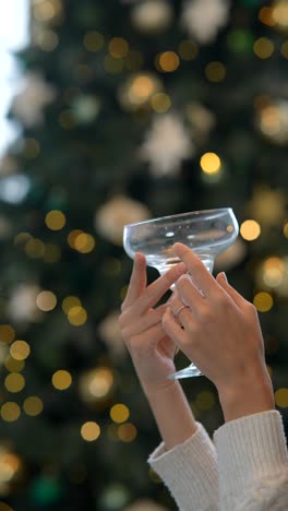 woman holding a cocktail glass by a christmas tree