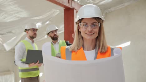 un joven ingeniero mira a la cámara en primer plano. retrato de un exitoso inversor inmobiliario de pie en el interior de un edificio vacío moderno con casco de seguridad y traje formal. concepto de ocupación de la gente.