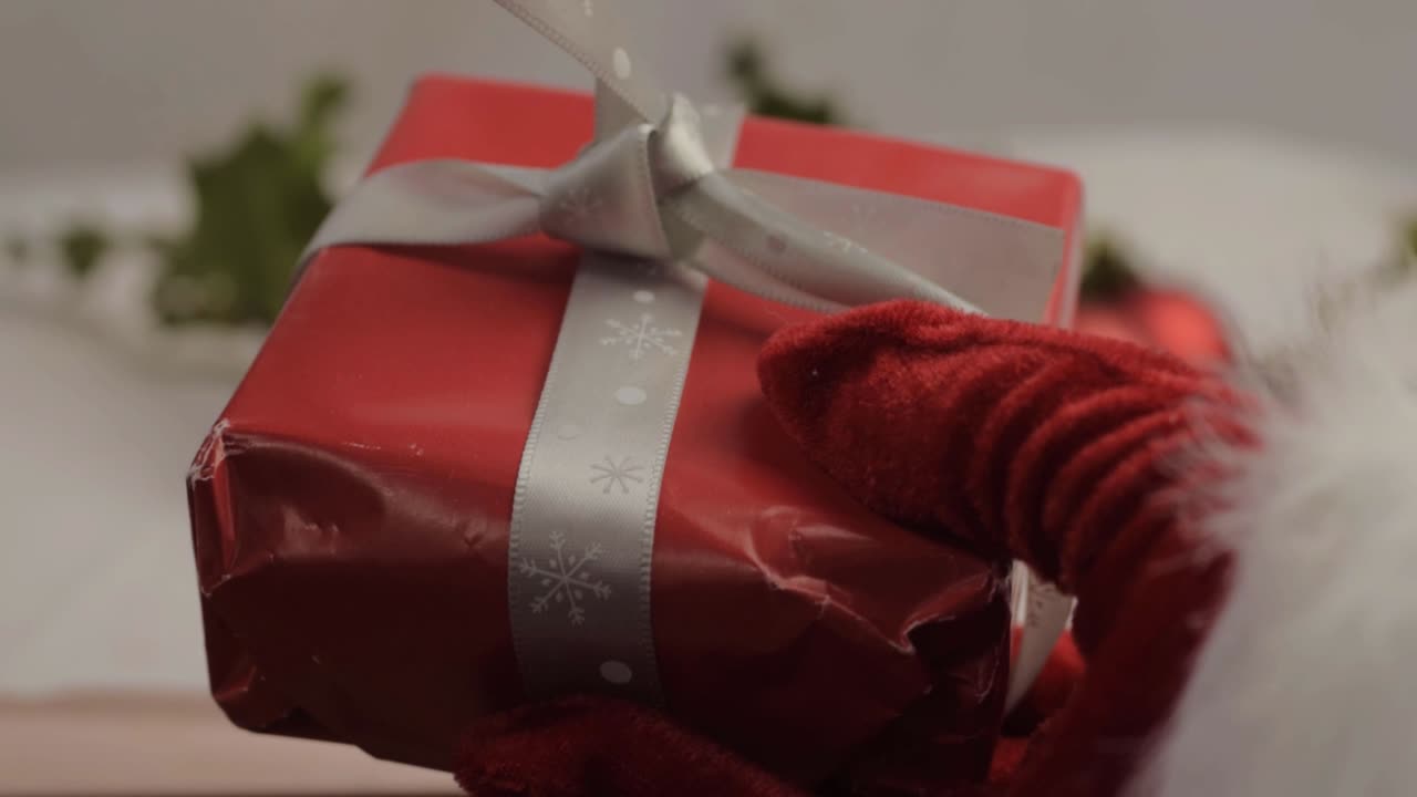 Hand in festive Santa style gloves holding a Christmas gift